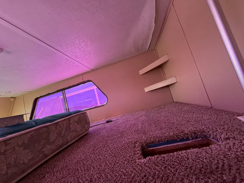 Slide: The Image of Interior of 1987 Three Buoys 5014 boat with carpet, mattress, and shelves under purple lighting. - 23