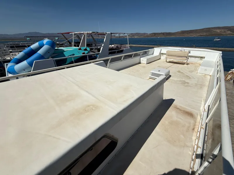 Slide: The Image of 1987 Three Buoys 5014 houseboat deck with seating, docked by a scenic lake. - 32