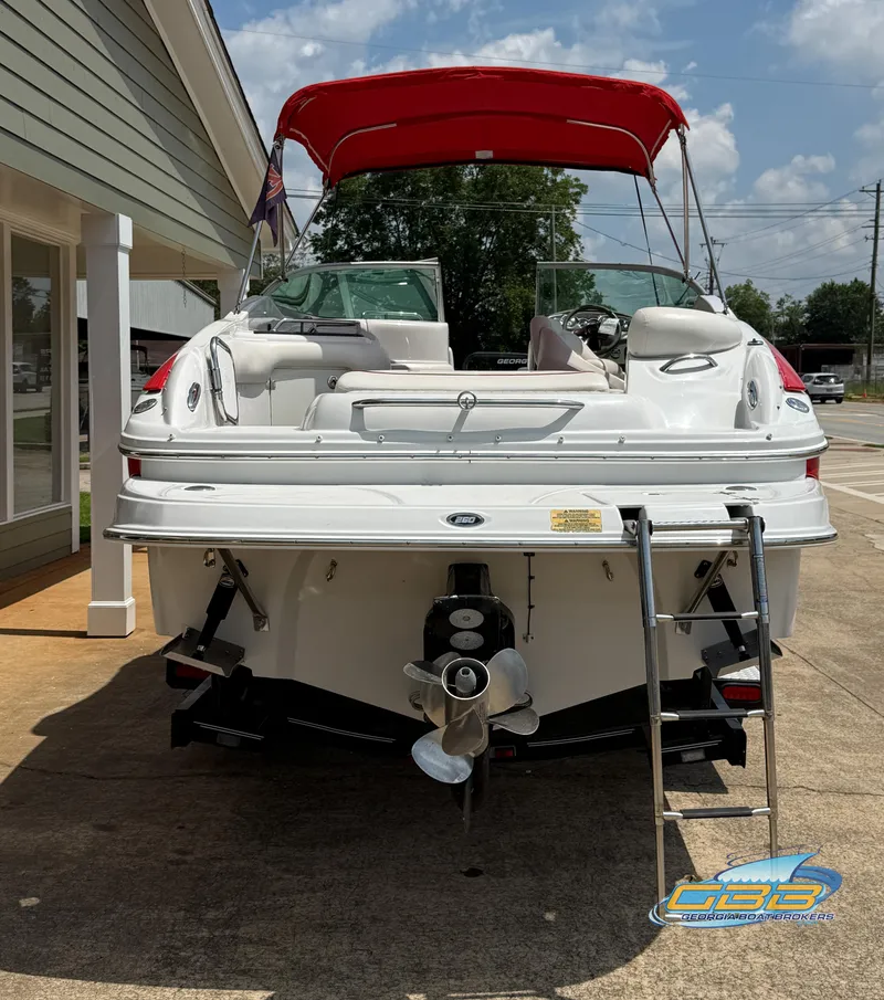 Slide: The Image of 2006 Crownline 260 EX boat with red canopy, rear view, parked on concrete. - 12