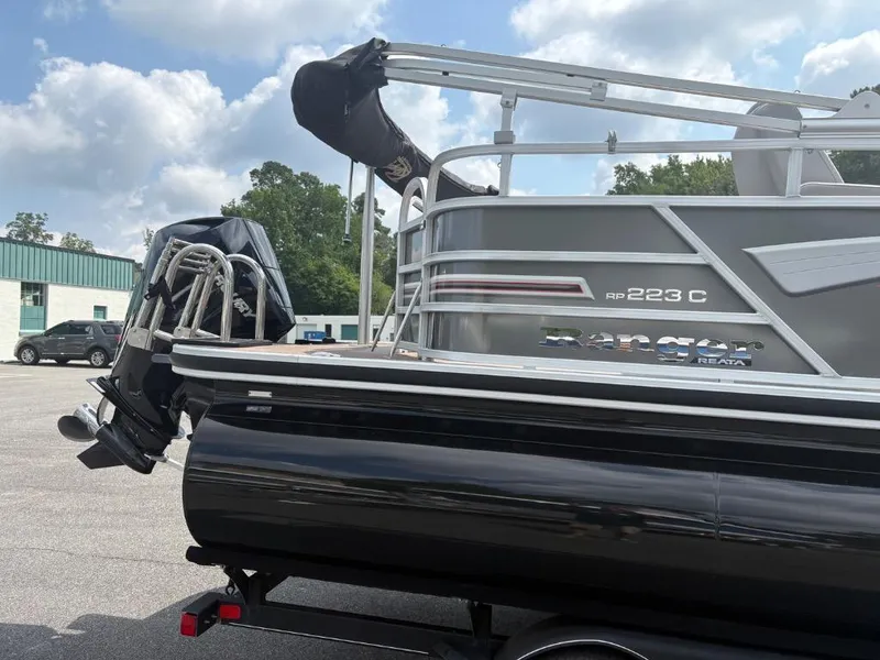 Slide: The Image of 2022 Ranger Reata 223C pontoon boat on trailer, parked outdoors under cloudy sky. - 4