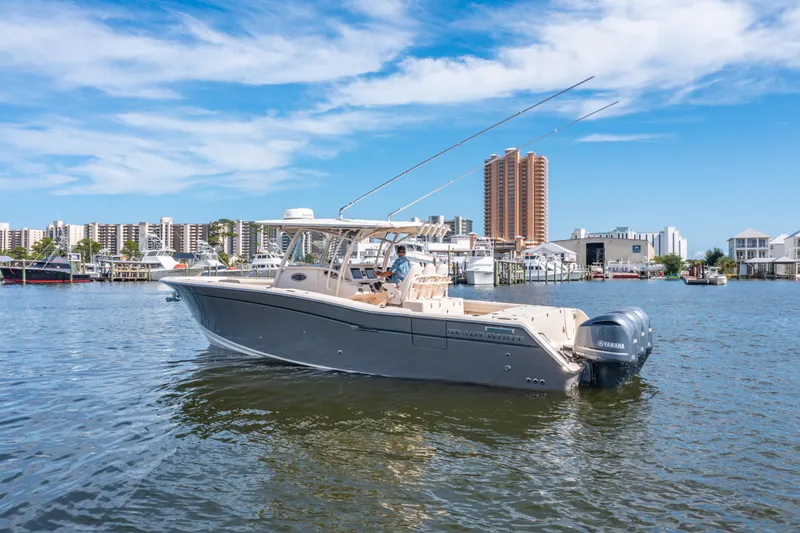 Slide: The Image of 2017 Grady-White 336 Canyon boat cruising in a marina with city skyline backdrop. - 6