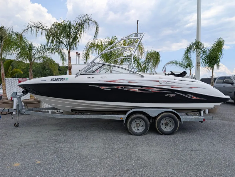 The Image of 2004 Yamaha AR230 HO boat on trailer, parked near palm trees under a cloudy sky. - 1