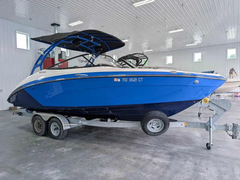 Slide: The Image of 2019 Yamaha Boats 242X E-Series in a garage, blue and white, on a trailer. - 2