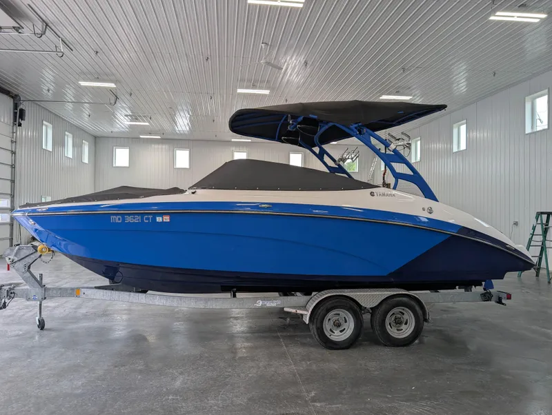 Slide: The Image of 2019 Yamaha Boats 242X E-Series in a garage, blue and white exterior, on a trailer. - 27