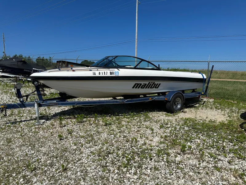 The Image of 1999 Malibu 20 Response LX boat on trailer, parked on gravel lot under clear blue sky. - 0