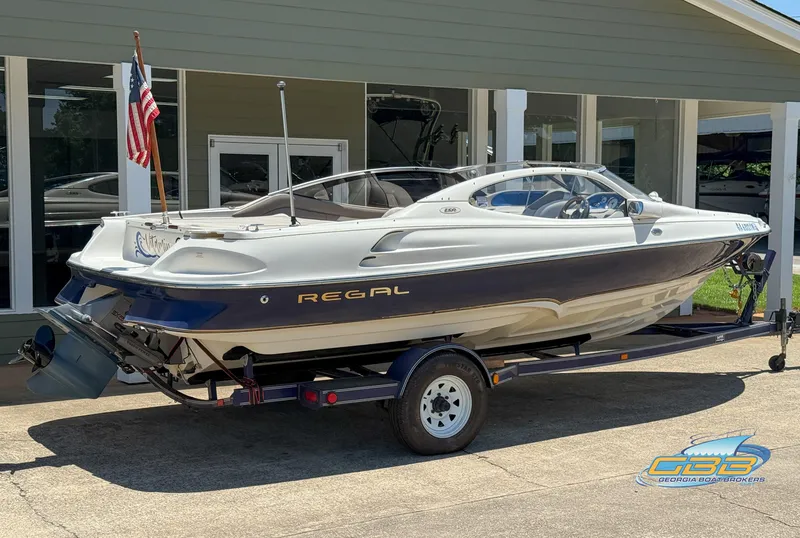 Slide: The Image of 1998 Regal 2100 LSR boat on trailer, parked outside a building with an American flag. - 7