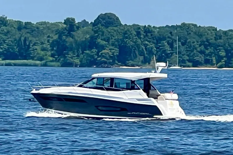 The Image of 2020 Regal 38 Grande Coupe cruising on a scenic lake with lush green shoreline. - 0