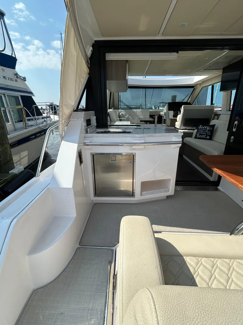 Slide: The Image of 2020 Regal 38 Grande Coupe yacht interior with seating and kitchenette, docked at marina. - 10