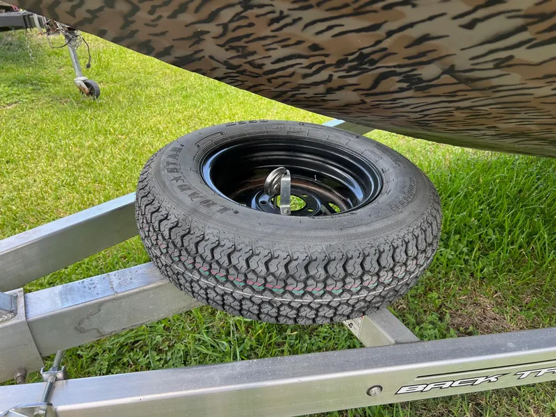 Slide: The Image of Spare tire mounted on a 2022 Xpress H190B boat trailer, parked on grass. - 15