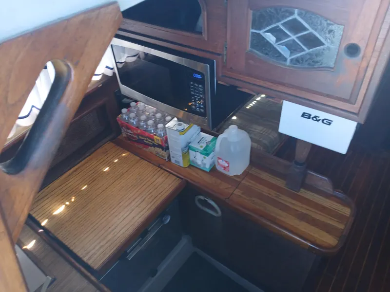 Slide: The Image of 1984 Newport Sailboat interior kitchen with microwave, wooden cabinets, and countertop supplies. - 11