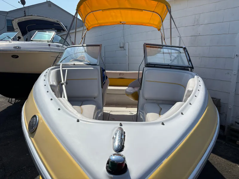 Slide: The Image of 2012 Crownline 185 SS boat with yellow canopy and white interior, docked beside another vessel. - 6