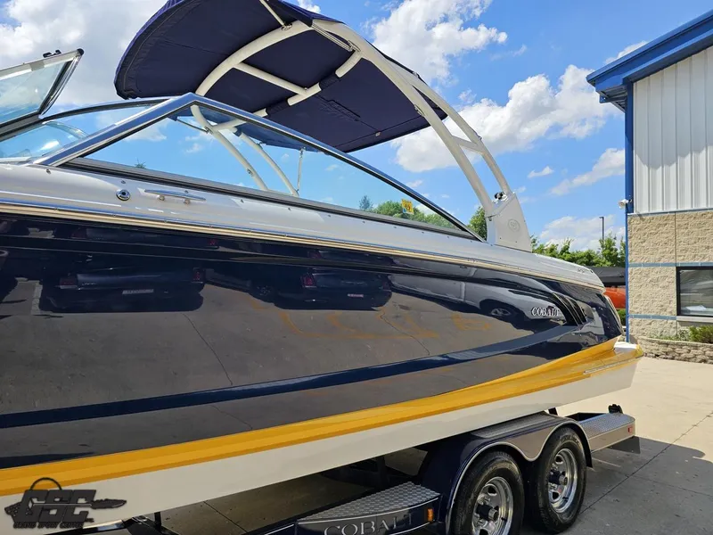 Slide: The Image of 2015 Cobalt A28 boat with blue hull and yellow stripe on trailer, sunny day. - 16