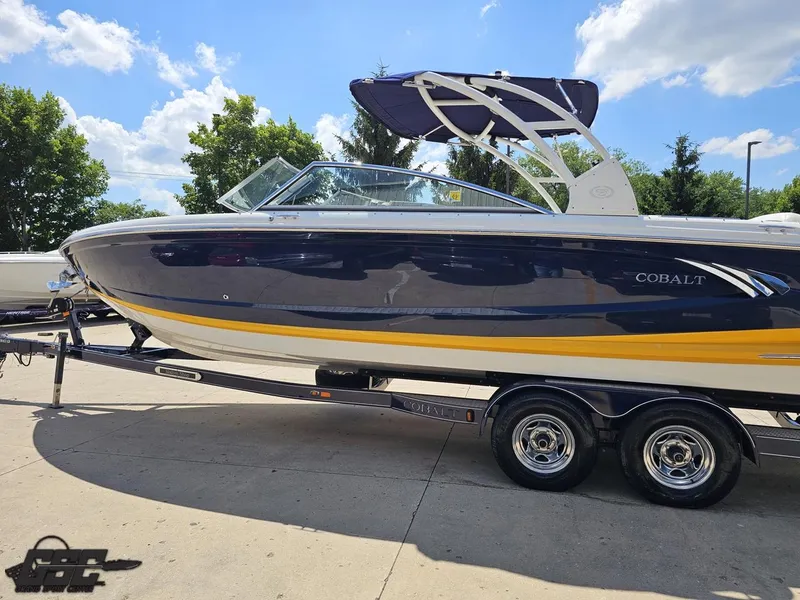 Slide: The Image of 2015 Cobalt A28 boat on trailer, blue and yellow design, sunny day background. - 19