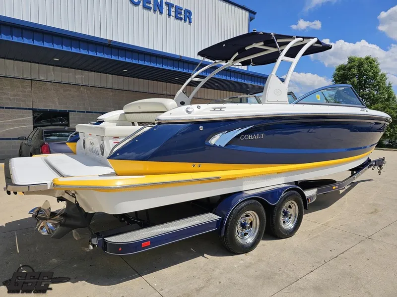 Slide: The Image of 2015 Cobalt A28 boat on trailer, blue and yellow design, parked outside a building. - 27