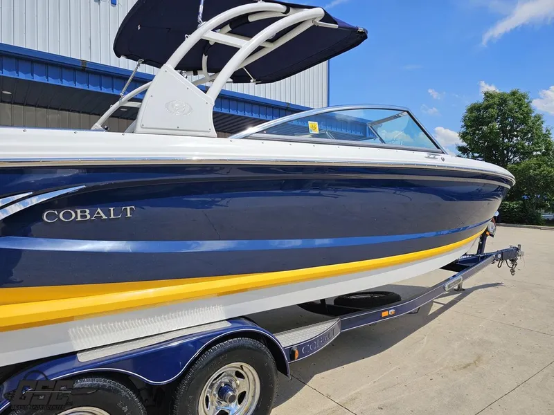 Slide: The Image of 2015 Cobalt A28 boat on trailer, blue and yellow design, sunny day. - 7
