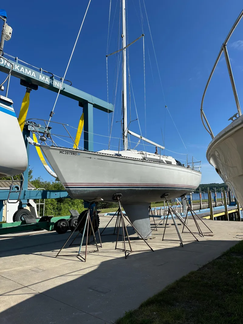 The Image of 1989 C&C 30 sailboat on stands at marina under clear blue sky. - 0