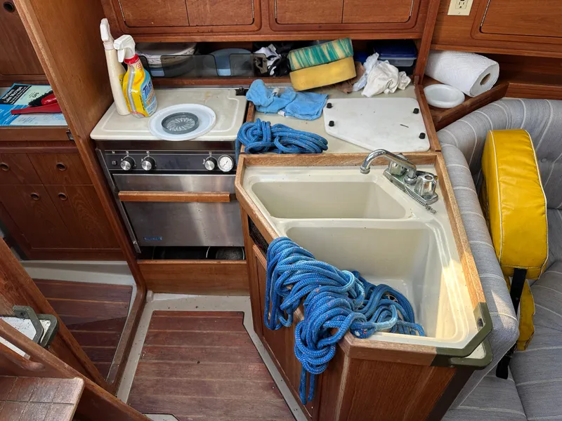 Slide: The Image of Interior of a 1989 C&C 30 sailboat kitchen with sink, stove, and cleaning supplies. - 32