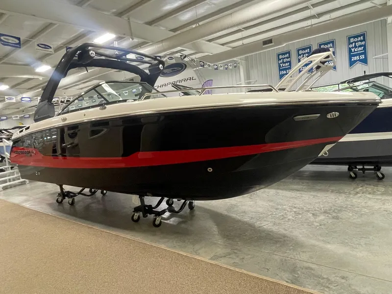Slide: The Image of 2025 Chaparral 26 Surf boat displayed indoors, featuring sleek black and red design. - 2
