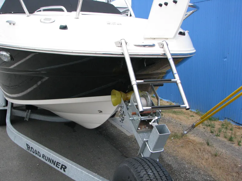Slide: The Image of 2017 Stingray 215 CR boat on trailer with ladder, parked near blue wall. - 2
