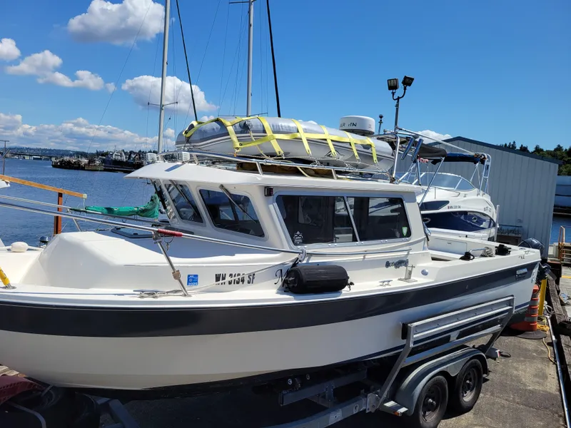 Slide: The Image of 2000 SeaSport 2400 XL Limited boat on trailer by waterfront, under clear blue sky. - 2