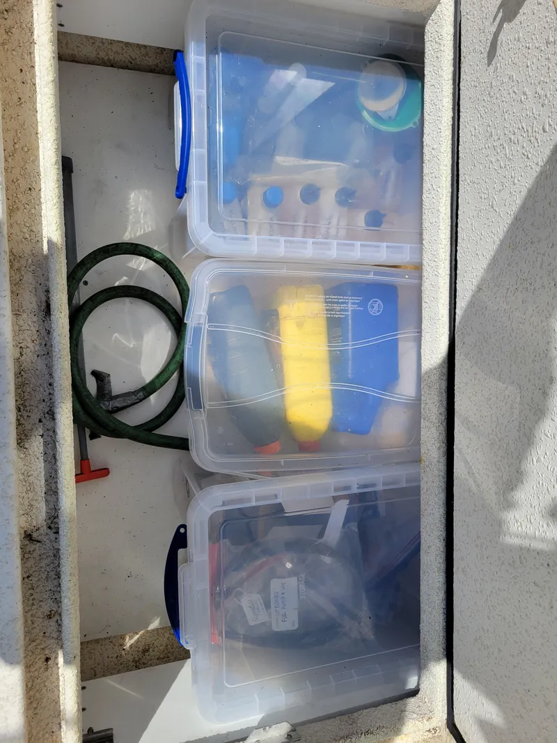 Slide: The Image of Storage compartment on a 2000 SeaSport 2400 XL Limited with organized plastic containers and a hose. - 37