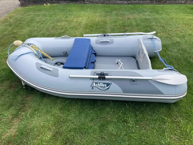 Slide: The Image of Inflatable Achilles boat on grass, featuring oars and blue seat cushion. - 46