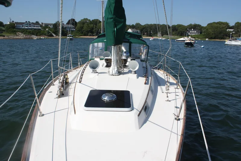 Slide: The Image of 1986 Sabre 34 MK II sailboat on calm water, with green sail cover and scenic shoreline. - 6