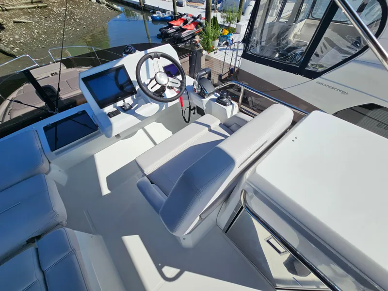 Slide: The Image of 2024 Beneteau Antares 12 helm station with modern controls and seating, docked by the water. - 10