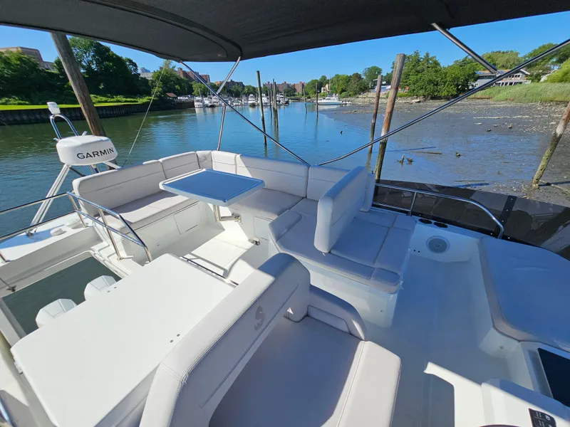 Slide: The Image of 2024 Beneteau Antares 12 yacht interior with seating and table, docked by a scenic river. - 13