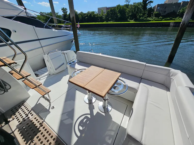 Slide: The Image of 2024 Beneteau Antares 12 yacht deck with seating and table, docked by a serene river. - 6