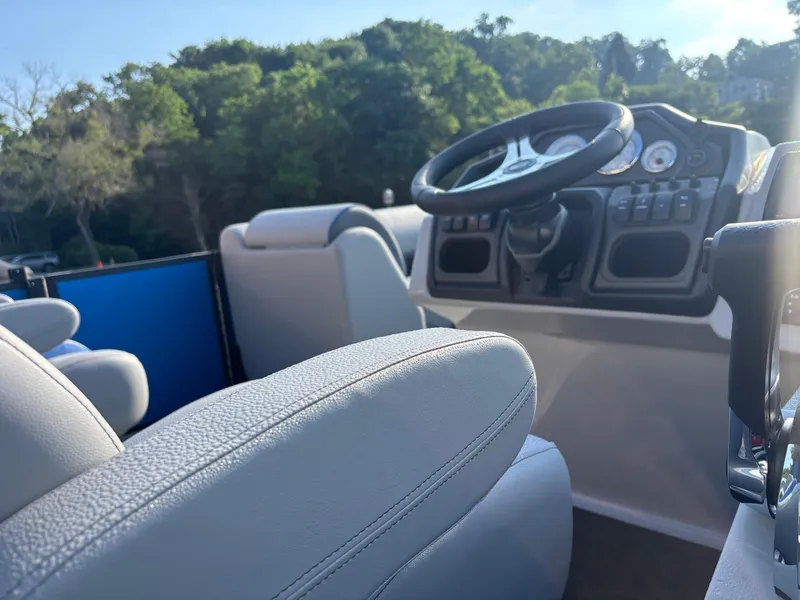 Slide: The Image of 2025 Bentley Pontoons Legacy Navigator interior with steering wheel and controls, surrounded by lush greenery. - 7