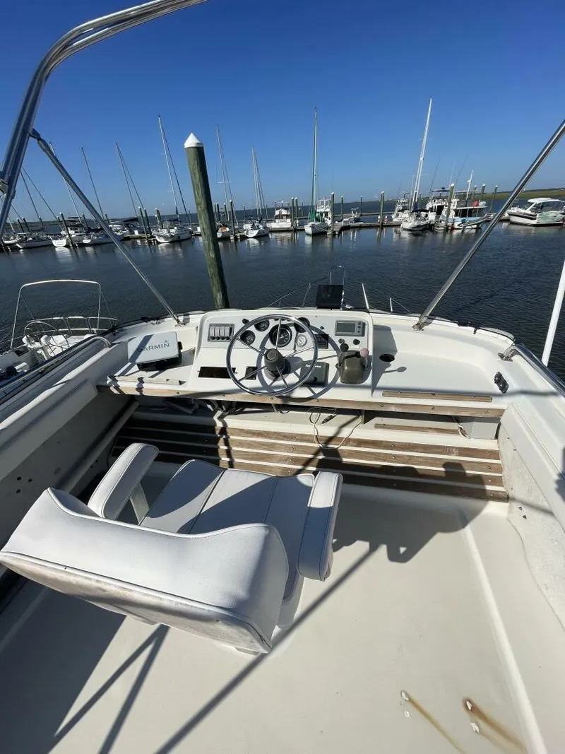 Slide: The Image of 1984 Mainship MK III boat helm with steering wheel, docked at marina under clear blue sky. - 22