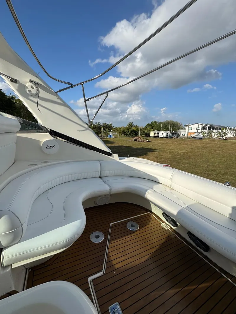 Slide: The Image of 2000 Cruisers Yachts 3870 Express interior with white seating and wooden deck under blue sky. - 16