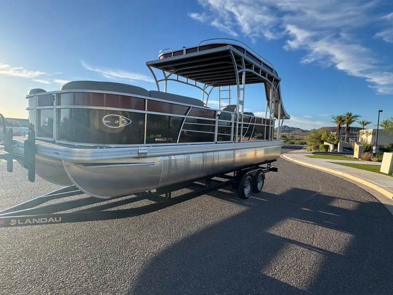 Slide: The Image of 2024 Landau Island Breeze 252 pontoon boat on trailer, parked on sunny street. - 3