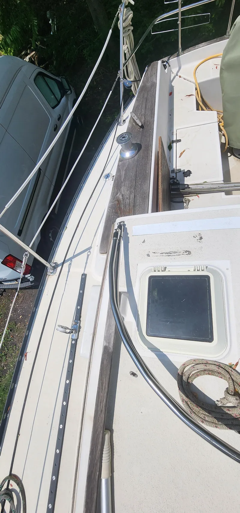 Slide: The Image of 1984 Caliber 28 sailboat deck with ropes and hatch, parked beside a white van. - 21