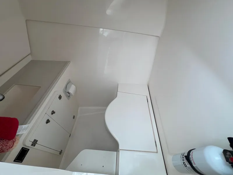 Slide: The Image of Interior of 2016 Pursuit 325 DC boat, featuring a compact bathroom with storage and fire extinguisher. - 34