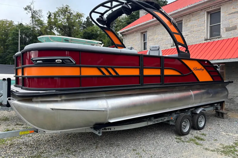 Slide: The Image of 2026 Bentley Pontoons Elite 223 Swingback with Wake Tower on trailer, vibrant red and orange design. - 3
