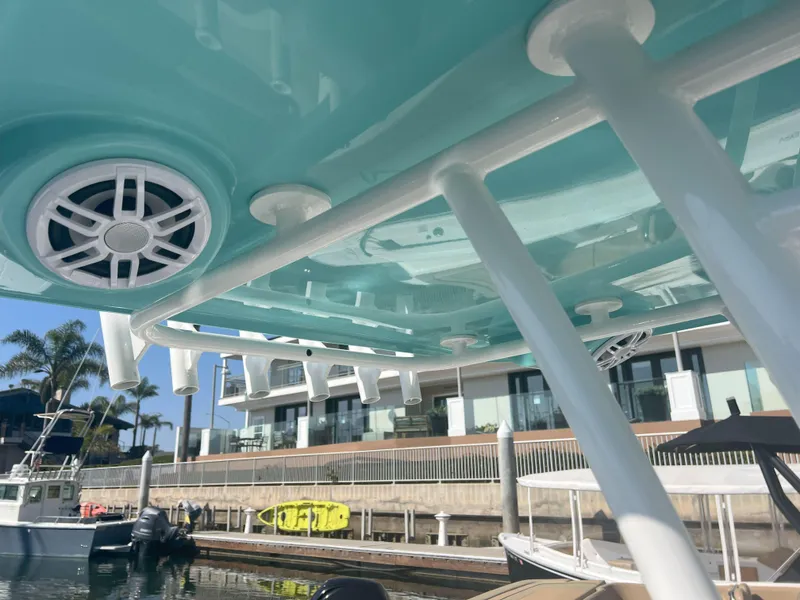 Slide: The Image of 2026 Reflex Gladiator 2400 boat with teal canopy and speaker, docked near waterfront homes. - 32