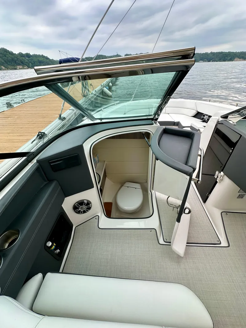 Slide: The Image of 2023 Regal 2800 Bowrider boat interior with open bathroom door, docked by a lake. - 9