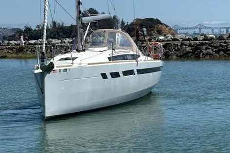 Slide: The Image of 2021 Jeanneau Sun Odyssey 349 sailboat navigating calm waters near a rocky shoreline. - 2