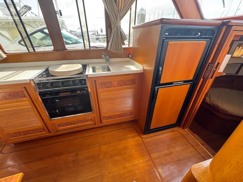 Slide: The Image of 2003 President Performance Trawler kitchen with stove, sink, and refrigerator, featuring wood cabinetry. - 4