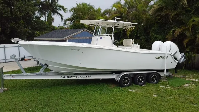 Slide: The Image of 2011 Mako 284 CC boat on trailer, parked on grass, surrounded by trees. - 7