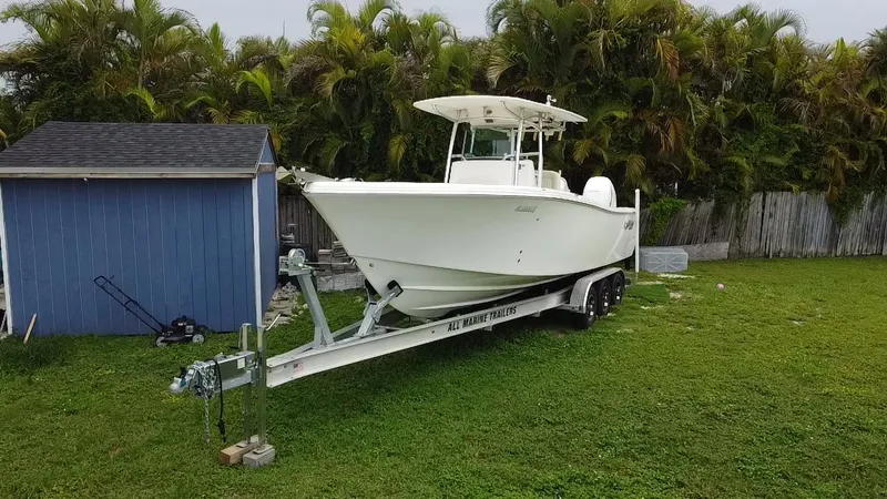 Slide: The Image of 2011 Mako 284 CC boat on trailer beside blue shed, surrounded by greenery. - 8