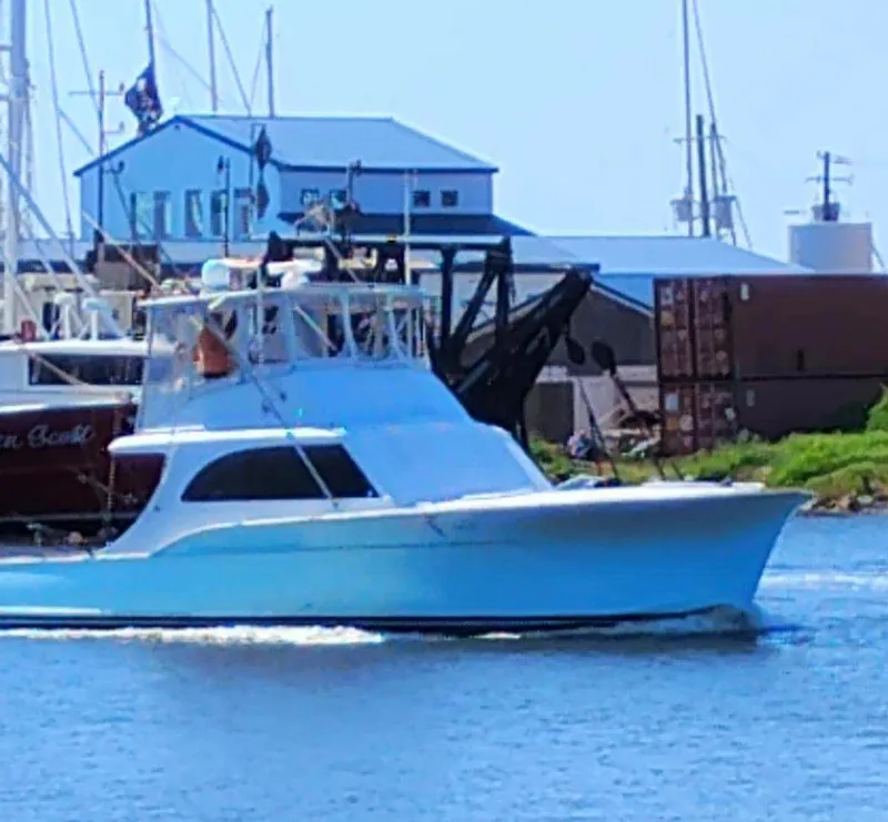 The Image of 1979 Buddy Davis 46 Convertible boat cruising in a marina with buildings in the background. - 0