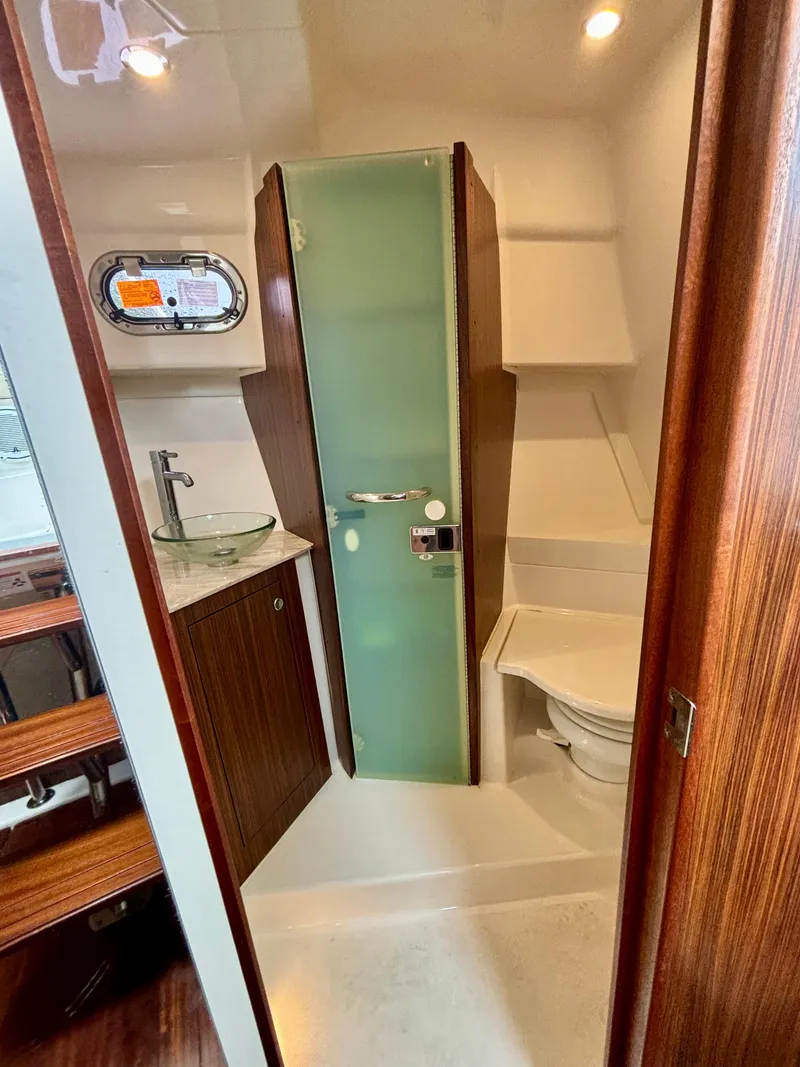 Slide: The Image of 2018 Pursuit OS 355 Offshore boat bathroom with glass sink, shower, and toilet. - 12