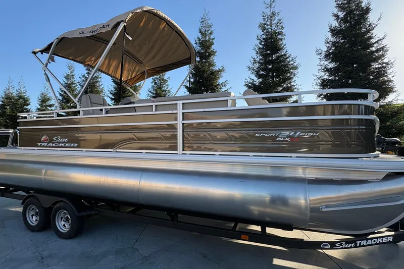 Slide: The Image of 2025 Sun Tracker Sportfish 24 XP3 pontoon boat on trailer, surrounded by trees. - 63