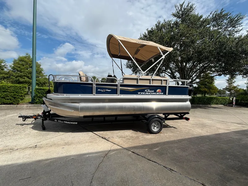 The Image of 2025 Sun Tracker Bass Buggy 18 DLX pontoon boat on trailer, parked outdoors. - 0