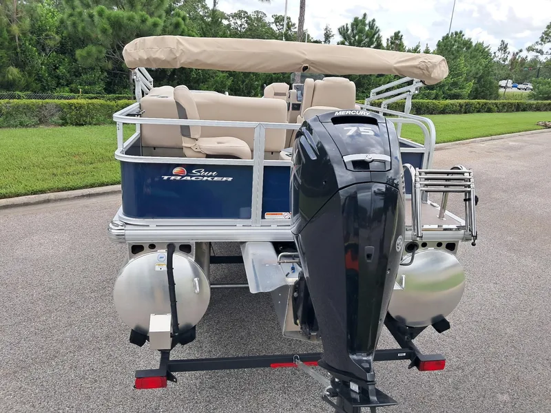 Slide: The Image of 2025 Sun Tracker Bass Buggy 18 DLX pontoon boat with Mercury 75 engine, parked on pavement. - 2