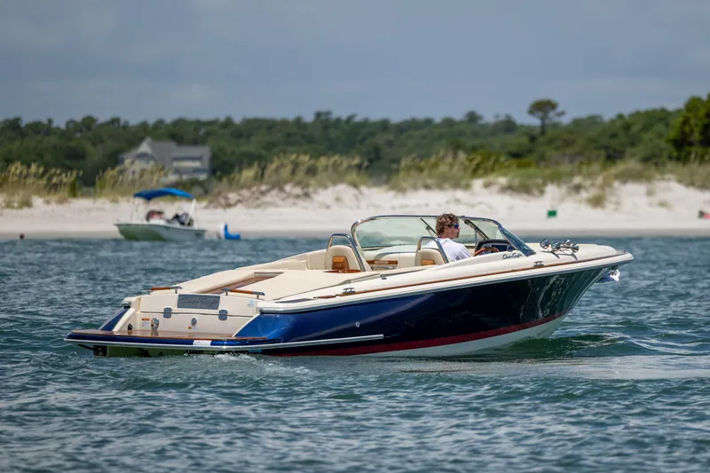 Slide: The Image of 2022 Chris-Craft Launch 27 boat cruising near a sandy beach with lush greenery. - 4