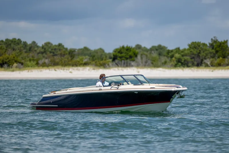 Slide: The Image of 2022 Chris-Craft Launch 27 boat cruising on water near a sandy shoreline. - 6